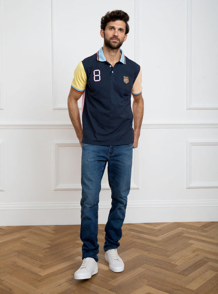 Man wearing navy based multicoloured panelled 100% cotton polo shirt with giant number 8 on pale pink back.